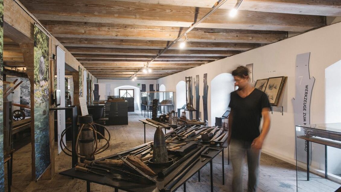 Ein Ausstellungsraum mit verschiedenen historischen Werkzeugen und Ausstellungsstücken. Eine Person steht in der Mitte und betrachtet die Exponate. | © Stefan Leitner