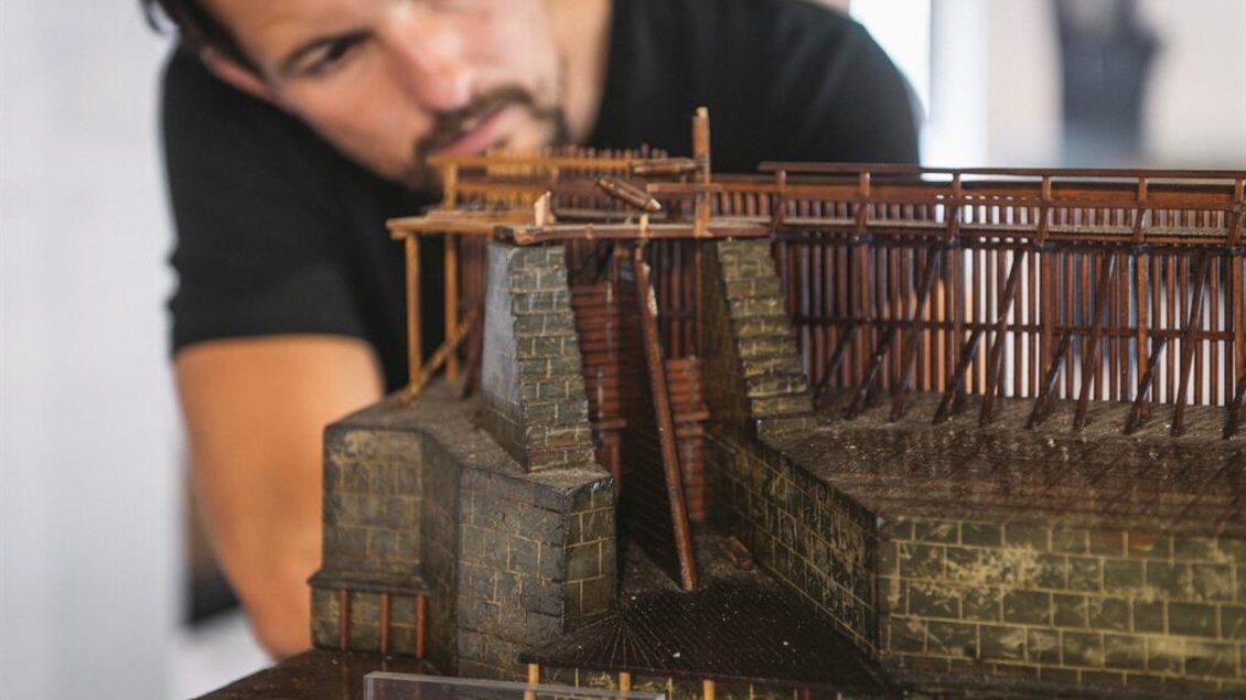 Ein Mann betrachtet ein detailliertes Modell einer historischen Struktur. Das Modell zeigt Holz- und Steinarchitektur mit einer Treppe. | © Stefan Leitner