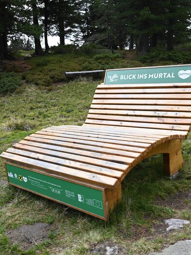 Eine Liege steht auf einer grünen Wiese neben einem kleinen Teich. Im Hintergrund sind Bäume und sanfte Hügel sichtbar. | © Anita Fössl