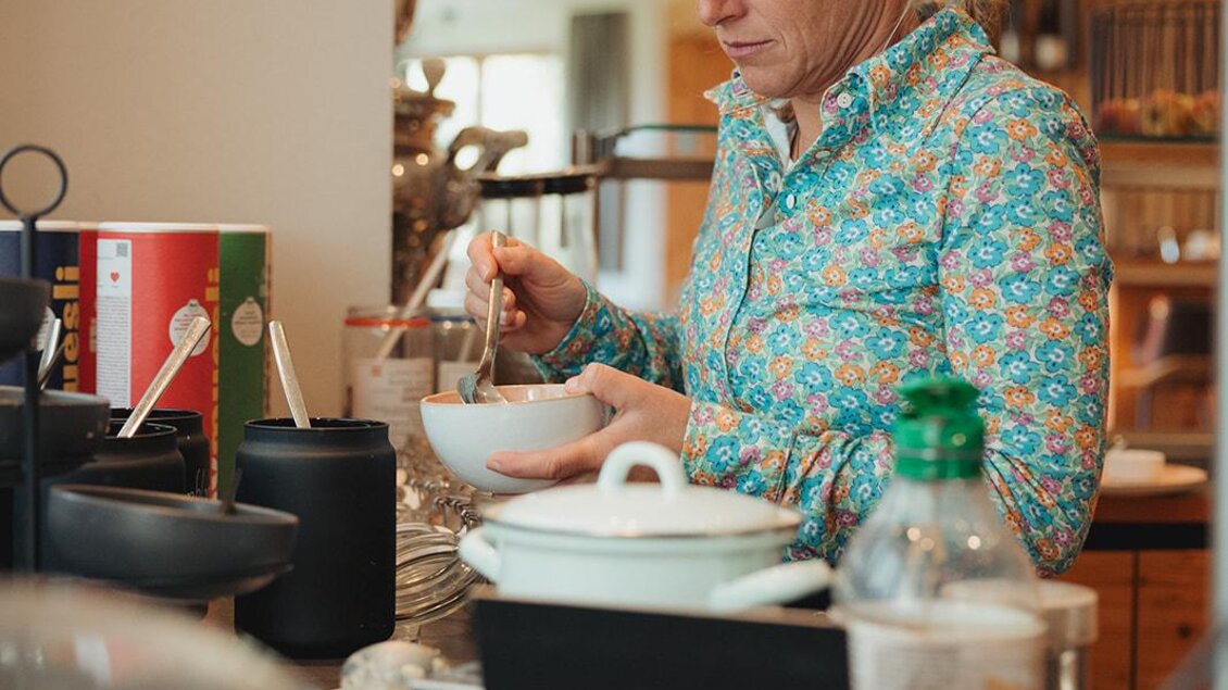 Eine Frau bereitet eine Mahlzeit in einer modernen Küche vor. Im Hintergrund sind verschiedene Küchengeräte und Zutaten sichtbar.