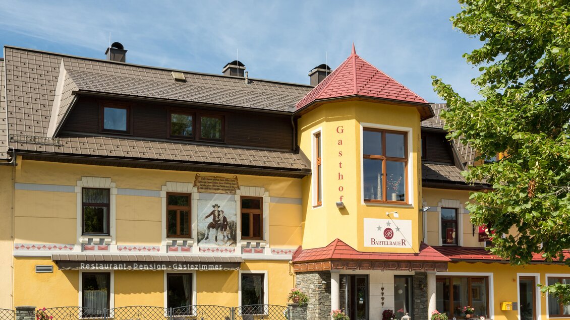 Ein charmantes Gasthaus mit gelber Fassade und rotem Dach. Vor dem Gebäude sind Bäume und eine einladende Terrasse. | © Fred Lindmoser