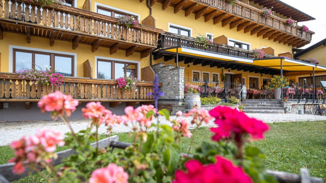 Ein charmantes Haus mit einem Balkons im oberbayerischen Stil, umgeben von bunten Blumen. Der Außenbereich lädt zum Verweilen und Entspannen ein. | © Fred Lindmoser