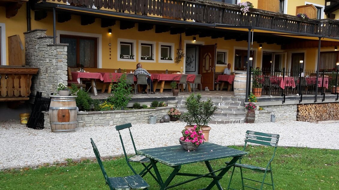 Ein charmantes Gasthaus mit Terrasse und Tischen im Freien. Die Umgebung ist grün und freundlich, ideal zum Entspannen. | © Gasthof Bartelbauer