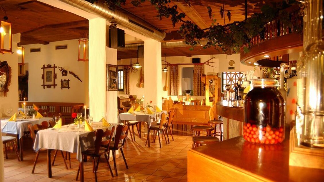 Ein gemütliches Restaurant mit holzgetäfeltem Interieur und Tischdecken in Weiß. Die warme Beleuchtung schafft eine einladende Atmosphäre.