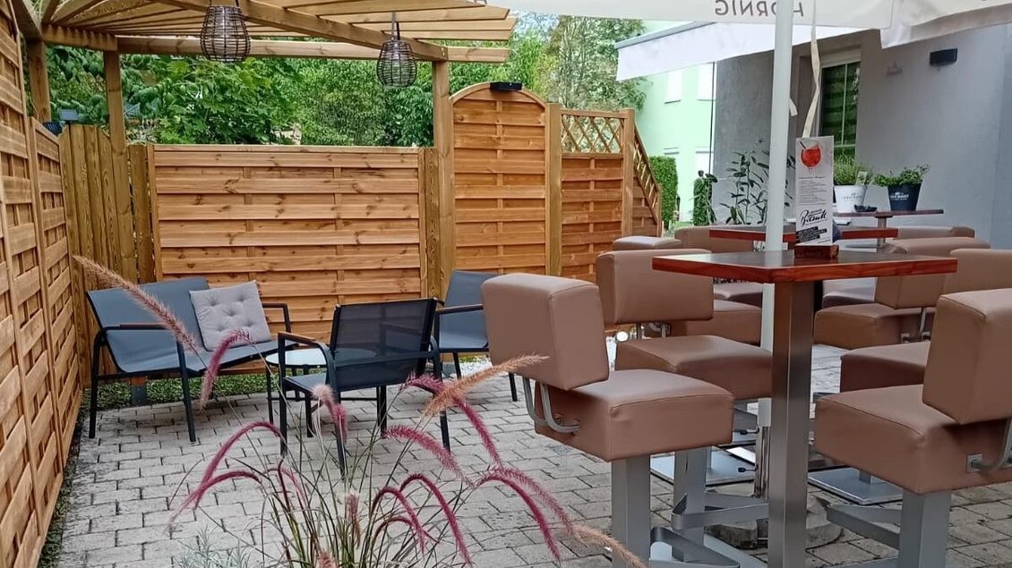 Moderner Sitzbereich mit Sonnenschirm im Außenbereich von Fredl’s Poolbar in Voitsberg. | © Fredl’s Poolbar