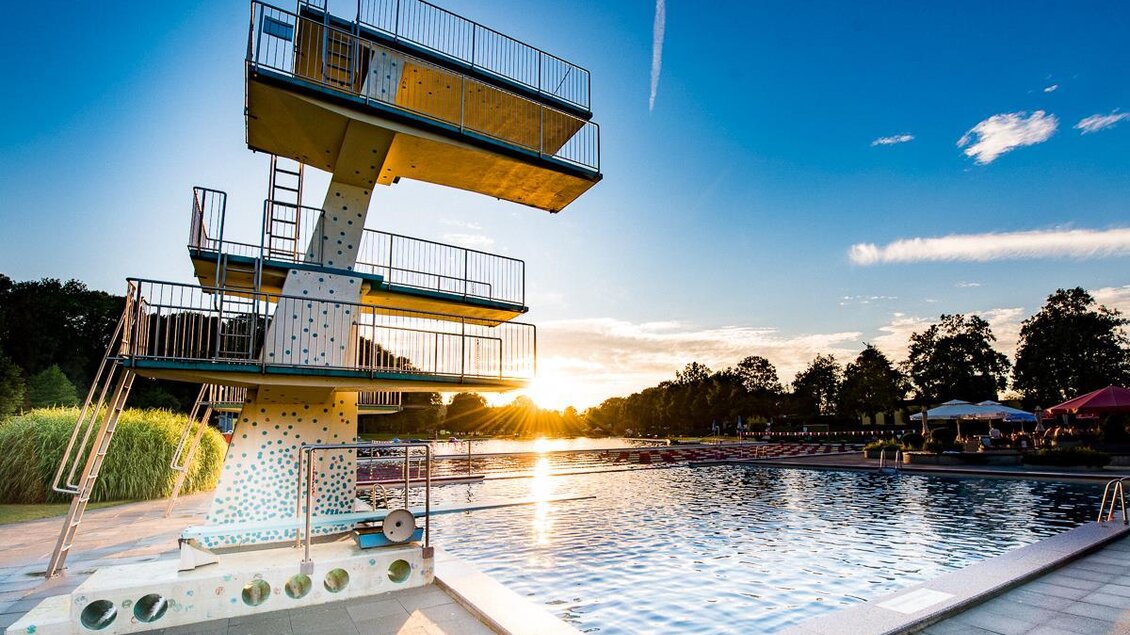 Ein Schwimmbad mit einem Sprungturm und einer sonnigen Abendstimmung. Im Hintergrund sind Bäume und Liegen zu sehen. | © Tourismusverband Thermen- & Vulkanland