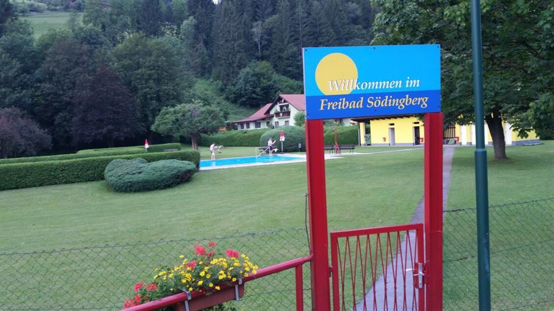 Ein Freibad mit einer grünen Wiese und einem Pool im Hintergrund. Der Eingang ist mit einem Willkommen-Schild beschriftet. | © Johann Hiden
