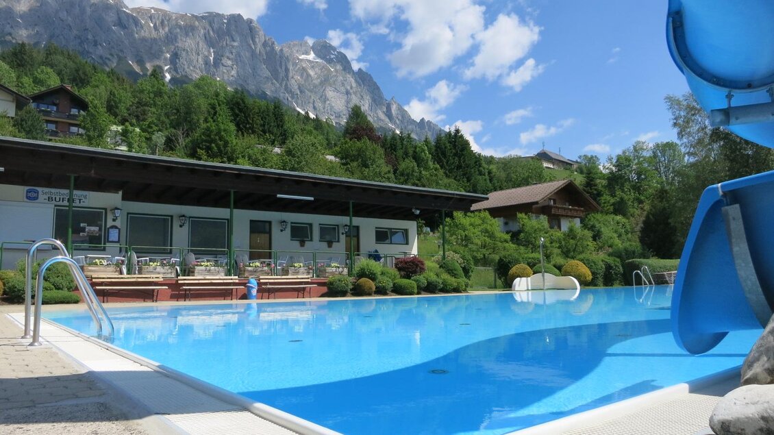 Ein schöner Swimmingpool mit blauen Wasser und einer Riesenrutsche. Im Hintergrund sind Berge und eine gepflegte Gartenlandschaft zu sehen. | © Gemeinde Mitterberg-Sankt Martin 