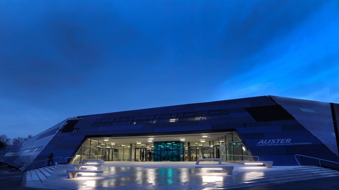 Ein modernes Gebäude mit einer futuristischen Architektur bei Dämmerung. Vor dem Eingang sind helle Stufen und ein reflektierender Boden. | © Holding Graz - Helge Sommer