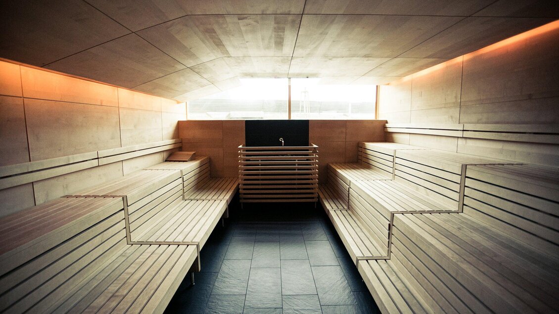 Ein modernes Saunainneres mit Holzbankreihen und sanfter Beleuchtung. Große Fenster sorgen für natürliches Licht und eine entspannende Atmosphäre. | © Holding Graz - Lupi Spuma