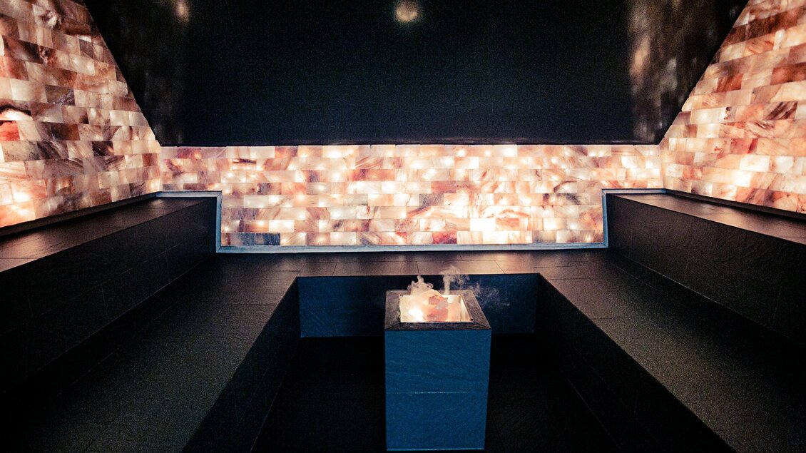 Ein entspannender Raum mit beleuchteten Wänden aus Salzsteinen. In der Mitte steht ein Tisch mit dampfender Wärmequelle. | © Holding Graz - Lupi Spuma