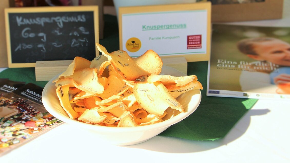 Ein Teller mit knusprigen Chips steht auf einem Tisch. Im Hintergrund sind Info-Karten und eine Tafel zu sehen. | © Schilcherland Spezialitäten
