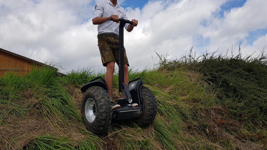 Ein junger Mann steht auf einem All-Terrain-Scooter auf einem Hügel. Im Hintergrund sind Gras und ein blauer Himmel mit Wolken zu sehen. | © Hotel-Restaurant Perschler