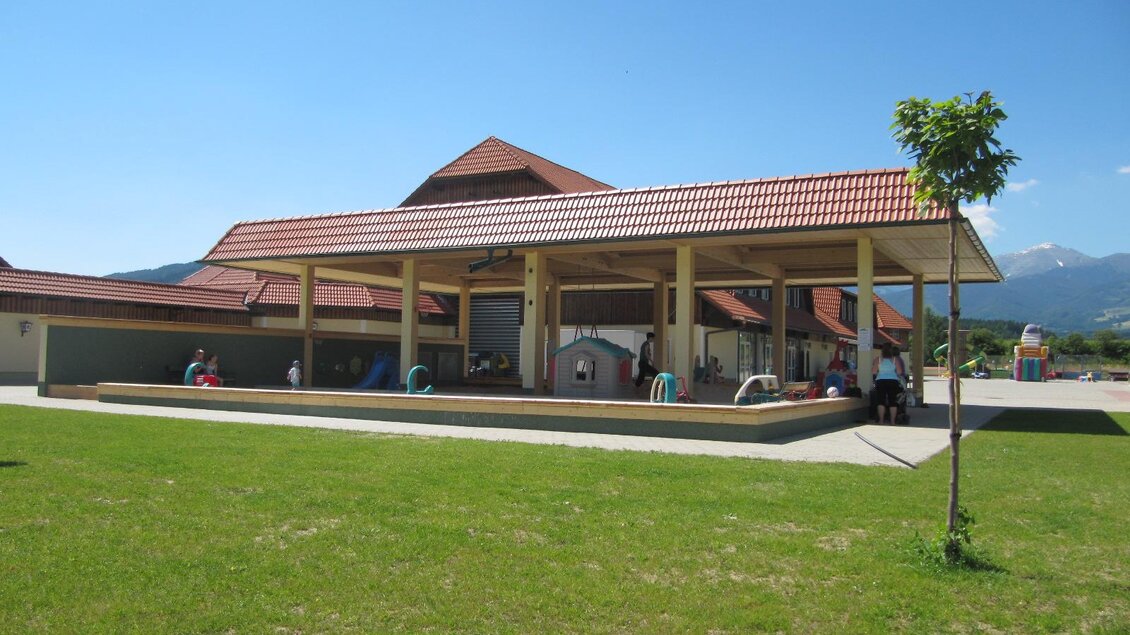 Ein modernes Gebäude mit rotem Dach steht in einer grünen Landschaft. Es gibt einen offenen Bereich mit Menschen, die sich dort aufhalten. | © Freizeitanlage Zechner