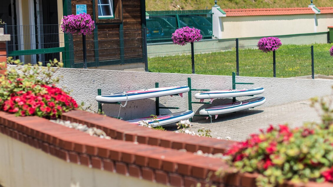 Ein schöner Außenbereich mit bunten Blumen und einer gemütlichen Atmosphäre. Im Hintergrund sind Surfbretter zu sehen, die auf einem Platz liegen. | © Freizeitanlage Zechner