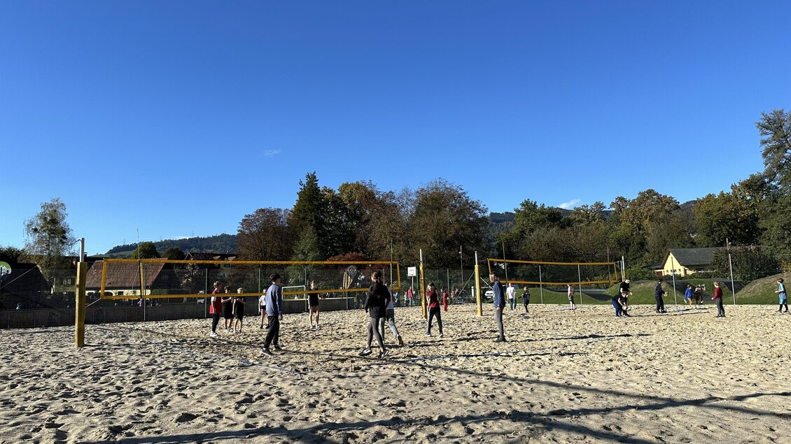 Ein Sandvolleyballplatz mit vielen Spielern. Der Himmel ist klar und blau, umgeben von Bäumen und etwas Landschaft. | © Stadtgemeinde Deutschlandsberg | E. Kleindienst