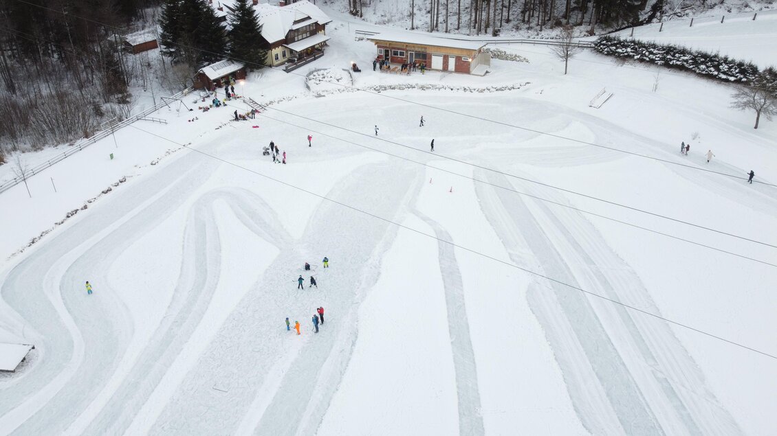 Eine verschneite Fläche mit mehreren Skifahrern und Schlittschuhläufern. Im Hintergrund sind Gebäude und Bäume zu sehen. | © Gemeinde Wald am Schoberpaß