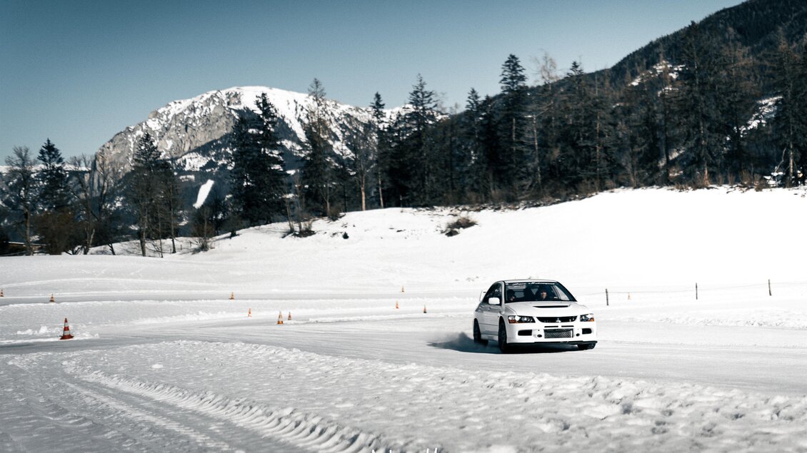 Ein Auto fährt auf einer verschneiten Strecke in den Bergen. Die Landschaft ist von Schnee und Bäumen umgeben. | © Hannes Zenz