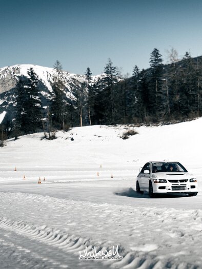 A car drives on a snowy road in the mountains. The landscape is surrounded by snow and trees. | © Hannes Zenz