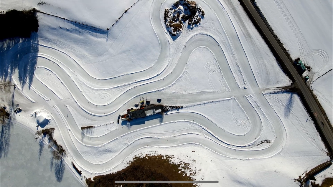 Eine kurvenreiche Schneepiste umgeben von weißen Feldern. Eine kleine Plattform ist im Bild sichtbar. | © Hannes Zenz