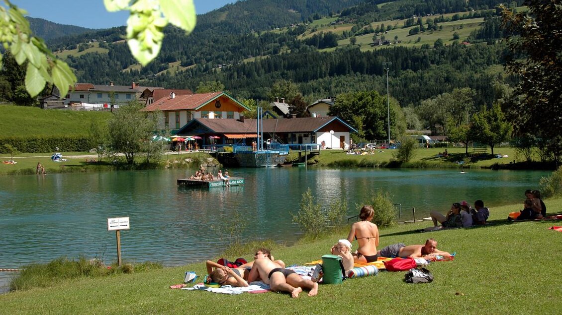 Ein schöner See mit Grünflächen und Sonnenliegen. Menschen entspannen am Ufer und genießen das Wetter. | © TVB Haus-Aich-Gössenberg