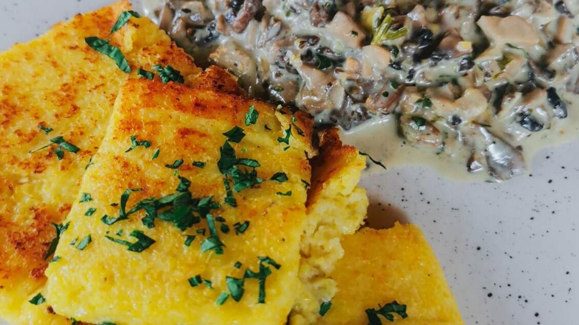 Ein Teller mit goldbraunem Polenta und einer cremigen Pilzsauce. Das Gericht ist mit frischer Petersilie garniert. | © Schuster Kulinarik OG