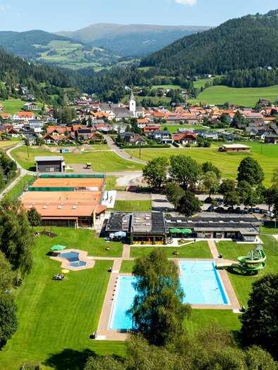 A tranquil landscape with a small village, surrounded by hills and forests. In the foreground, several pools and green meadows can be seen. | © TV Murau