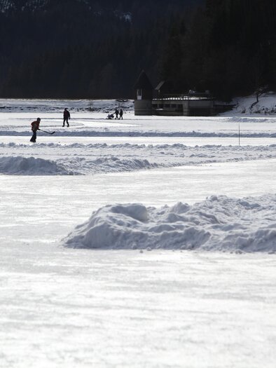 A winter landscape with frozen water and snow hills. People enjoy various activities on the ice. | © www.erzberg-leoben.at