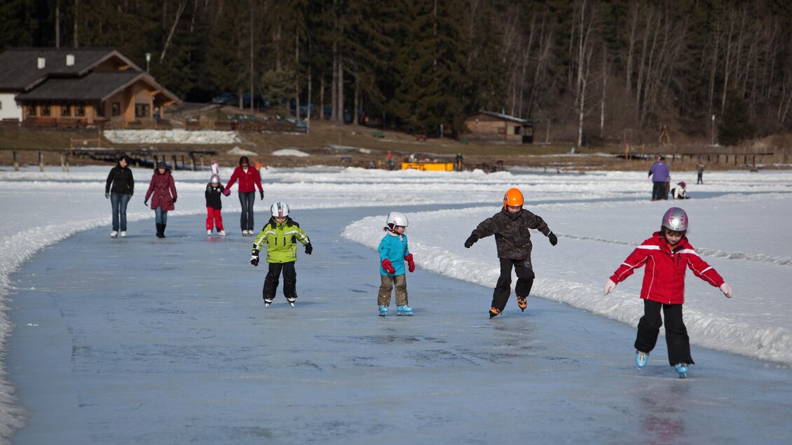 Eine Gruppe von Menschen läuft auf einer gefrorenen Eislaufbahn. Kinder und Erwachsene genießen das Eislaufen in einer winterlichen Landschaft. | © www.erzberg-leoben.at