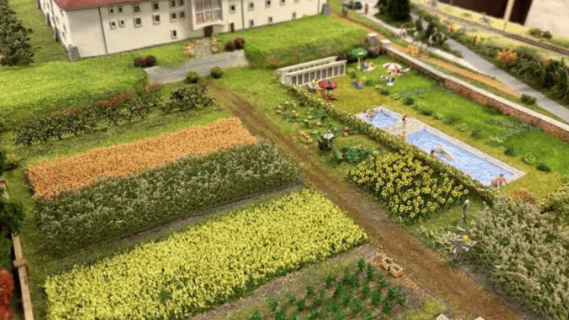 Eine detaillierte Modelllandschaft mit einem kleinen Gebäude, Gärten und einem Pool. Verschiedene landwirtschaftliche Felder sind in verschiedenen Farben angelegt. | © IG Freunde der Sulmtalbahn