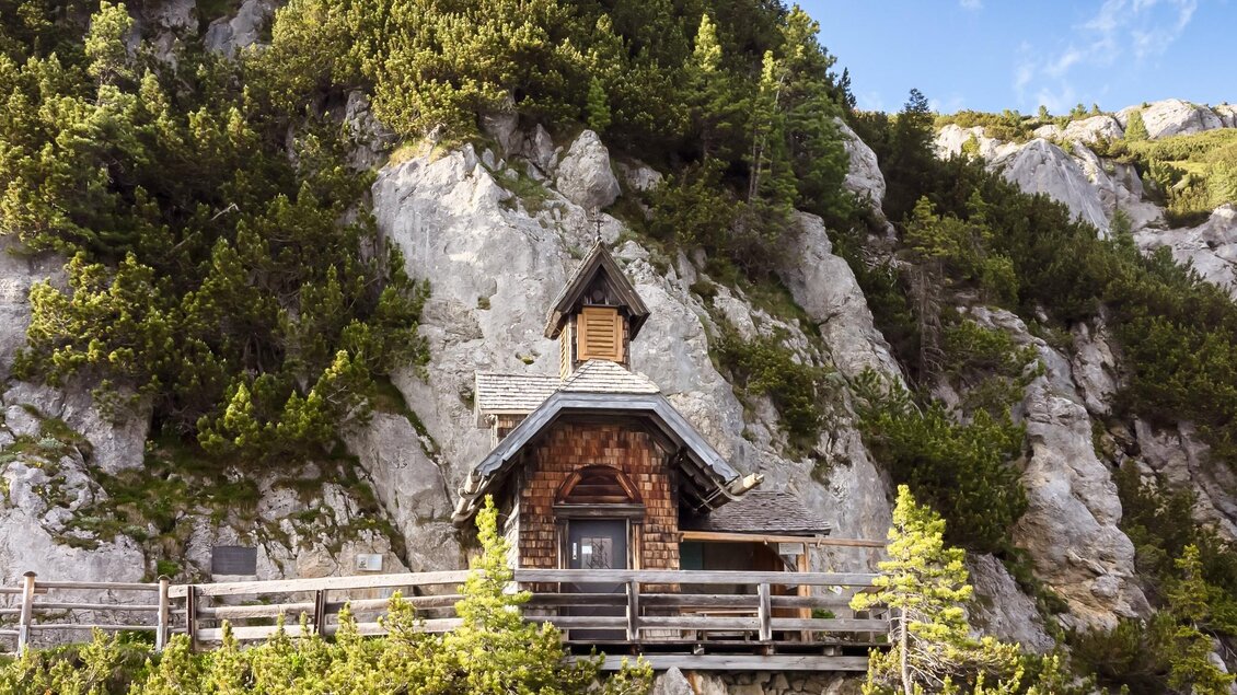 Ein charmantes, kleines Holzhaus auf einer Klippe, umgeben von grünen Bäumen. Im Hintergrund sind beeindruckende Felsen und ein blauer Himmel zu sehen. | © Schöttl/ORF