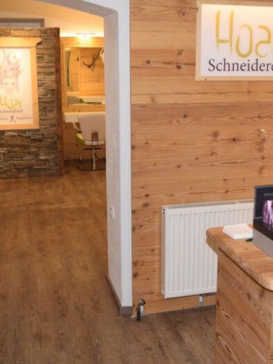 Ein moderner Friseursalon mit Holzverkleidung und einem einladenden Empfangsbereich. Im Hintergrund sind Stühle und ein dekoratives Bild zu sehen. | © Hoar-Schneiderei