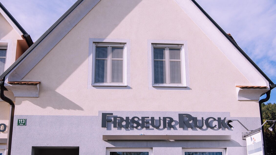 Ein Friseursalon mit der Beschriftung "Friseur Ruck". Das Gebäude ist hell und hat ein modernes design mit großen Fenstern. | © Kurkommission Bad Blumau
