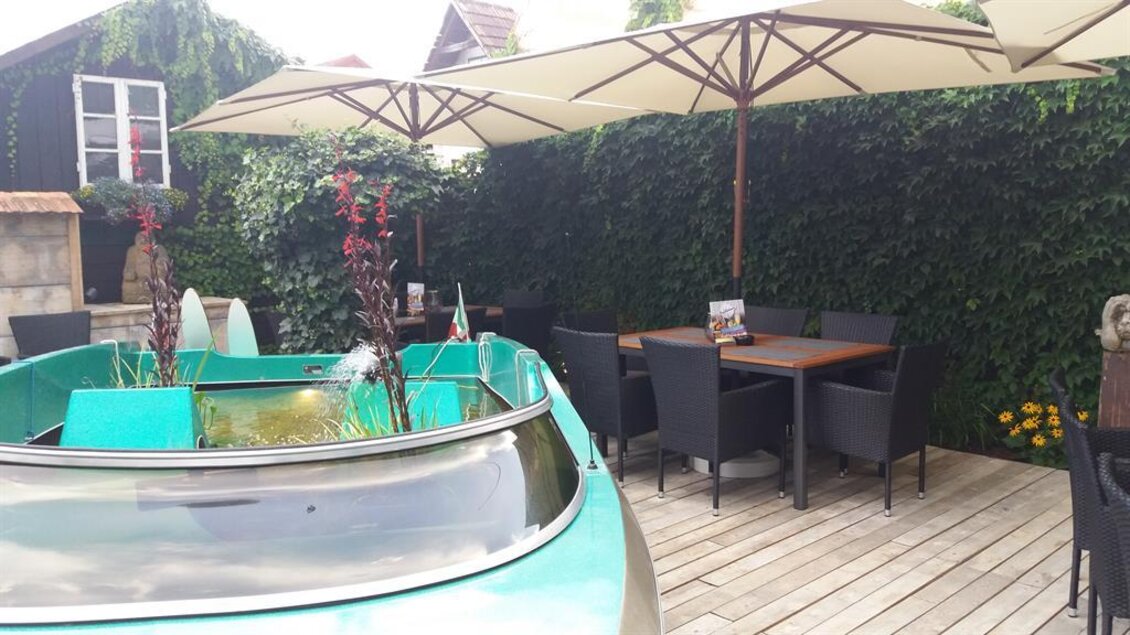 Ein gemütlicher Außensitzbereich mit einem grünen Boot und Holzdecks. Sonnenschirme und Pflanzen schaffen eine einladende Atmosphäre. | © TV Lipizzanerheimat/EU