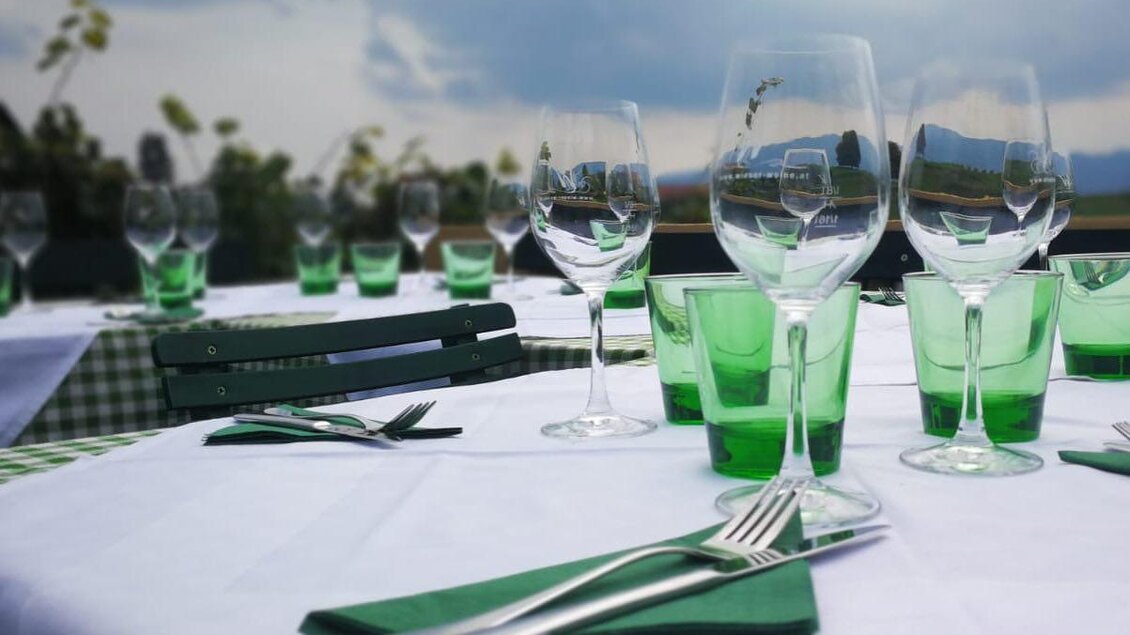 Eine schön gedeckte Tafel mit vielen Gläsern und Besteck. Der Tisch ist mit einem weißen Tuch und grünen Akzenten dekoriert.