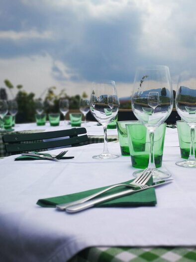 Eine schön gedeckte Tafel mit vielen Gläsern und Besteck. Der Tisch ist mit einem weißen Tuch und grünen Akzenten dekoriert.