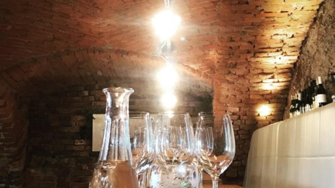 Ein stimmungsvolles Weinglas-Arrangement in einem stilvollen Keller. Die sanfte Beleuchtung und die Steinwand schaffen eine einladende Atmosphäre.