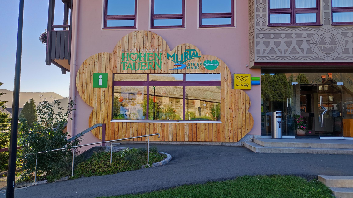 Ein informatives Büro mit einer Holztäfelung und einem bunten Schriftzug. Vor der Fassade gibt es eine grüne Wiese und einen gepflegten Weg. | © Marlene Zandl