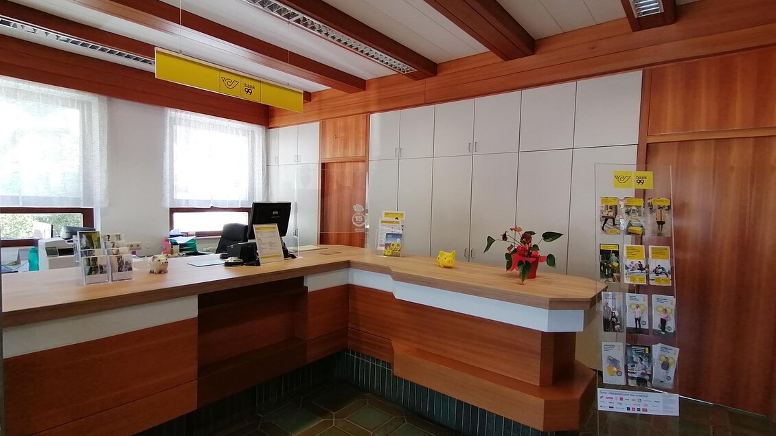 Ein Empfangsbereich mit Holzverkleidung und einem freundlichen Empfangstresen. Am Rand stehen Informationsmaterialien und eine Pflanze. | © Marlene Zandl