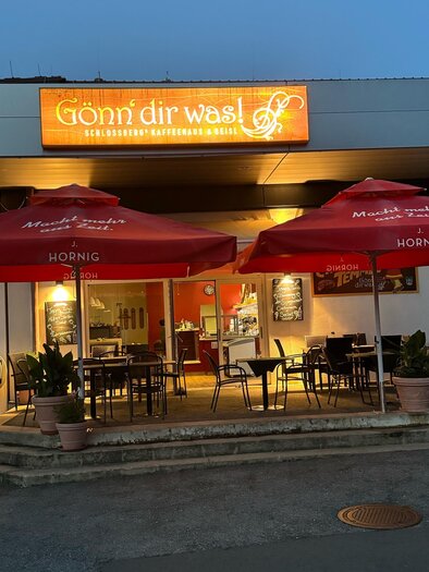 Ein gemütliches Restaurant mit roten Schirmen und Außenplätzen. Die einladende Leuchtschrift zeigt den Namen des Lokals. | © Gönn dir was