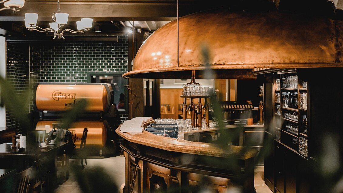 Eine moderne Bar mit einer kupfernen Theke und stilvollem Interieur. Grünpflanzen und gedämpftes Licht schaffen eine einladende Atmosphäre. | © Gösser Bräu - Tina Szabo