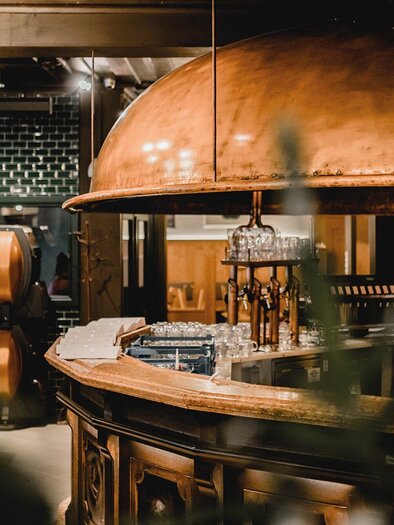Eine moderne Bar mit einer kupfernen Theke und stilvollem Interieur. Grünpflanzen und gedämpftes Licht schaffen eine einladende Atmosphäre. | © Gösser Bräu - Tina Szabo