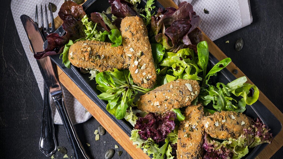 Ein Teller mit knusprigen Gemüsefrikadellen auf einem Bett aus frischem Salat. Der Anrichten ist ansprechend mit verschiedenen Blattsalaten und dekorativen Kürbiskernen. | © Gösser Bräu - Werner Krug