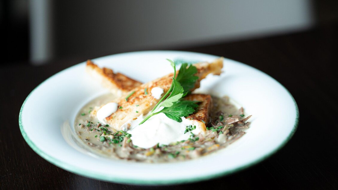 Ein Teller mit einer cremigen Suppe und knusprigem Brot. Frische Kräuter und ein Klecks Sauerrahm garnieren das Gericht. | © Gösser Bräu - Tina Szabo