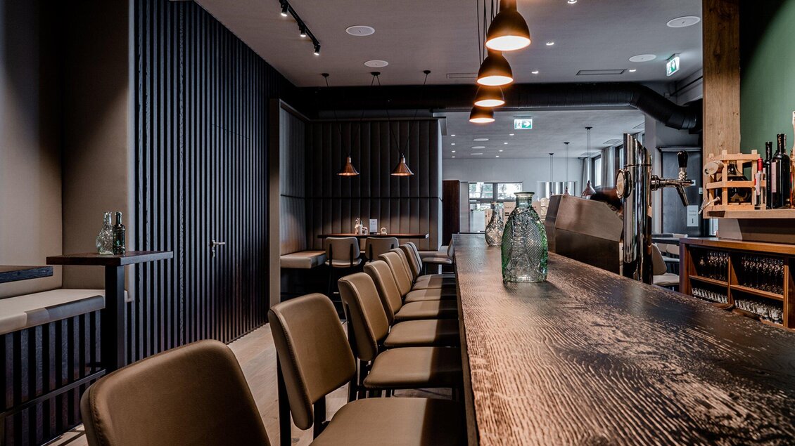 Ein modernes Restaurant mit einer langen Holzbar und eleganten Sitzplätzen. Die Wände sind dunkel gehalten und sanfte Beleuchtung schafft eine gemütliche Atmosphäre. | © Gösser Bräu - Tina Szabo