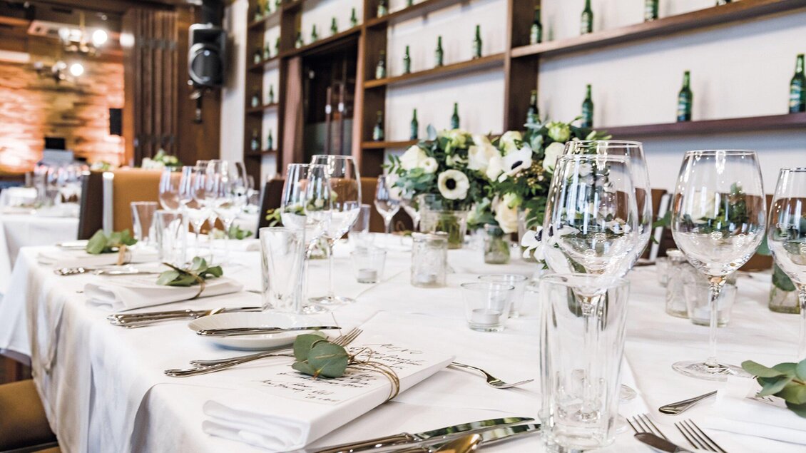 Ein elegant gedeckter Tisch mit Gläsern, Besteck und frischen Blumenarrangements. Die sanfte Beleuchtung schafft eine festliche Atmosphäre. | © Gösser Bräu - Werner Krug