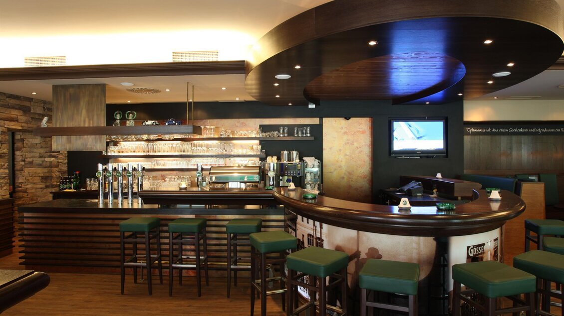 Eine elegante Bar mit einem runden Thekenbereich und hohen Stühlen. Die warme Beleuchtung und moderne Einrichtung schaffen eine einladende Atmosphäre. | © Brauunion Leoben