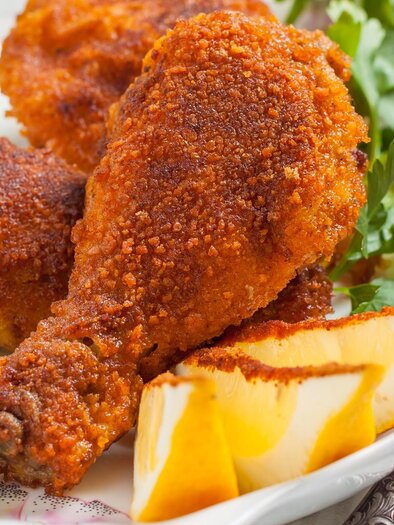 Fried chicken thighs on a plate, surrounded by fresh parsley. The crispy crust is golden brown and appetizing. | © Shutterstock - SEAGULL_L