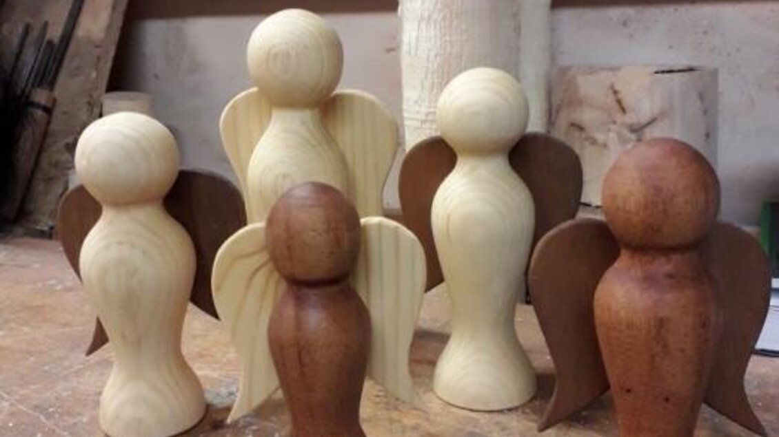 Sechs handgefertigte Holzengel stehen auf einem Tisch. Sie sind in verschiedenen Holzarten und Farben gefertigt.