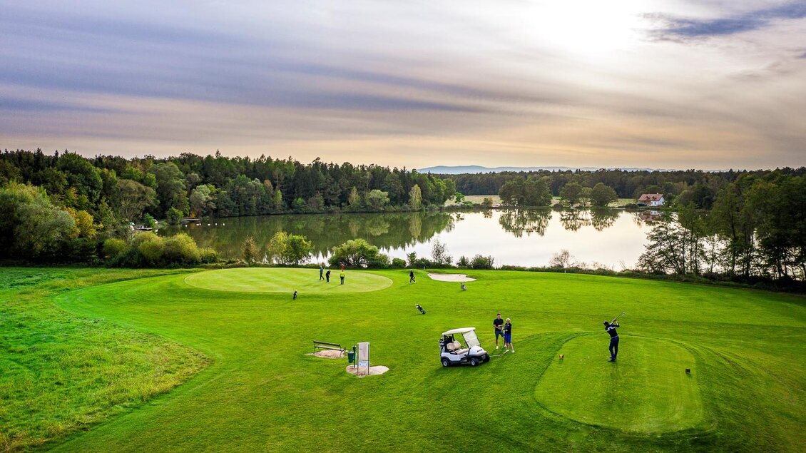 Eine malerische Golfanlage mit grünen Fairways und einem See im Hintergrund. Das sanfte Licht des Sonnenuntergangs sorgt für eine entspannte Atmosphäre. | © TV- Thermen- & Vulkanland